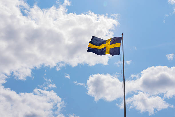 Swedish flag waving in the wind against a blue sky with fluffy white clouds