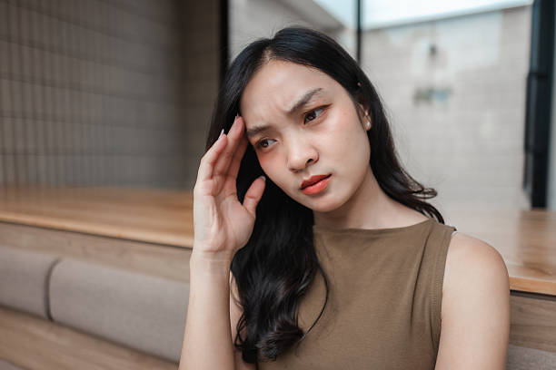 istock Young Asian woman suffering from a headache, touching her forehead with her hand, looking concerned and worried 2222097521