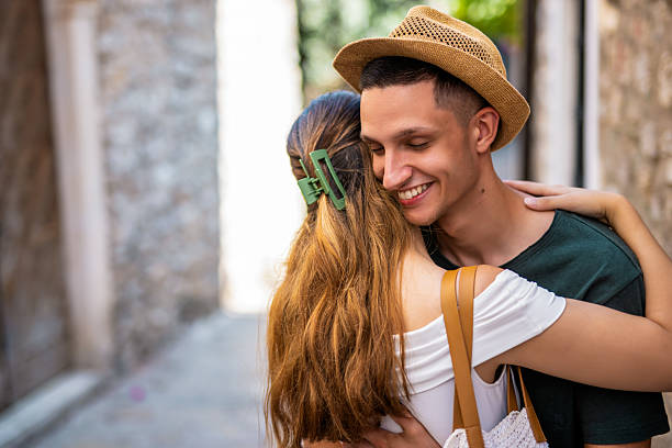 A young couple shares a tender embrace in a picturesque old town, with the focus on the boyfriend's happy expression.