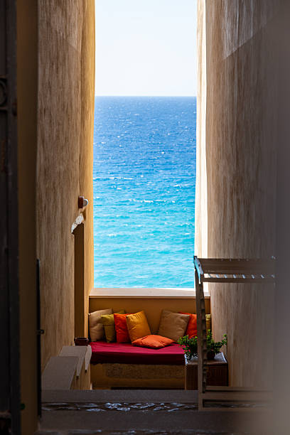 A narrow stone corridor in Tropea, Calabria opens to the sea, with a cushioned bench offering a vibrant view of turquoise waters.