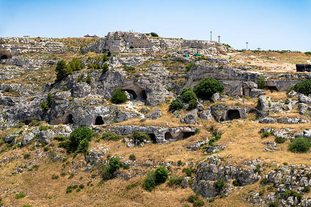View of ancient cave dwellings carved into a rocky hillside near Matera, Basilicata, showing openings and sparse vegetation.