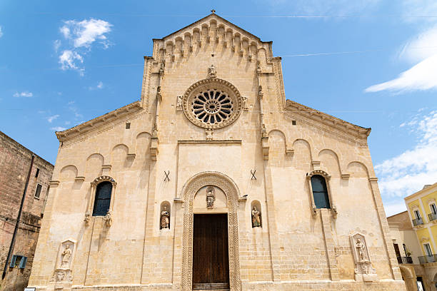 Front view of Romanesque church with rose window, arched doorway, carved statues, geometric details and light stone facade under blue sky.
