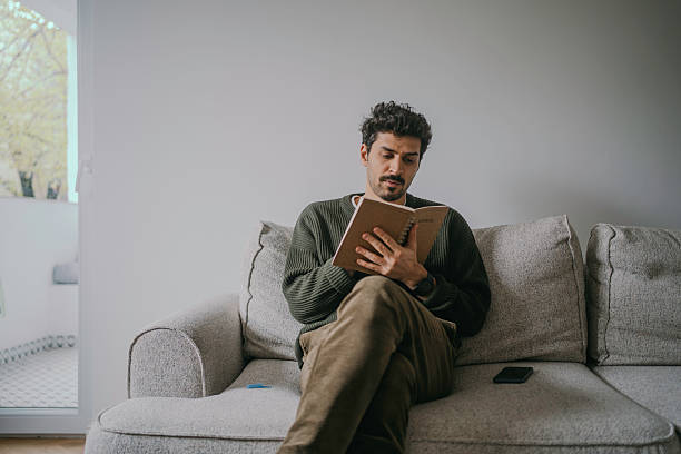 istock Thoughtful Young Handsome man sitting on the couch and journaling. 2222122229