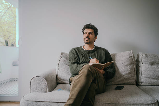 Thoughtful Young Handsome man sitting on the couch and journaling.