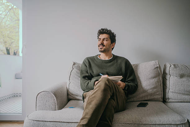 istock Thoughtful Young Handsome man sitting on the couch and journaling. 2222122234