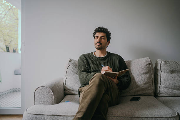 istock Thoughtful Young Handsome man sitting on the couch and journaling. 2222122276