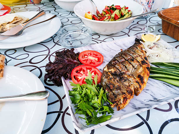 A plate with two steaks of fried pink salmon on a lettuce leaf with lemon and sauce on a light wooden table, cutlery is nearby. Top view, flat lay.