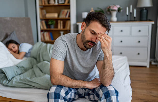 istock Sad man sitting on bed while wife is sleeping in bedroom 2222122917