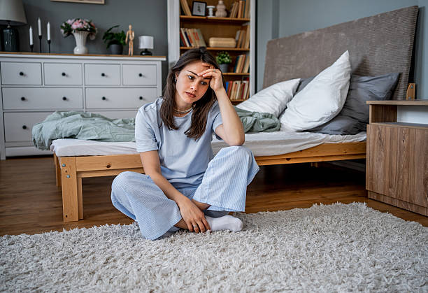 istock Sad young woman sitting on bedroom floor touching forehead 2222122988