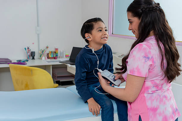 Young boy sits on examination table while a female audiologist performs a hearing test in a doctor's office, highlighting pediatric healthcare