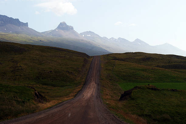 A solitary dirt road cuts through green hills towards misty Icelandic peaks.