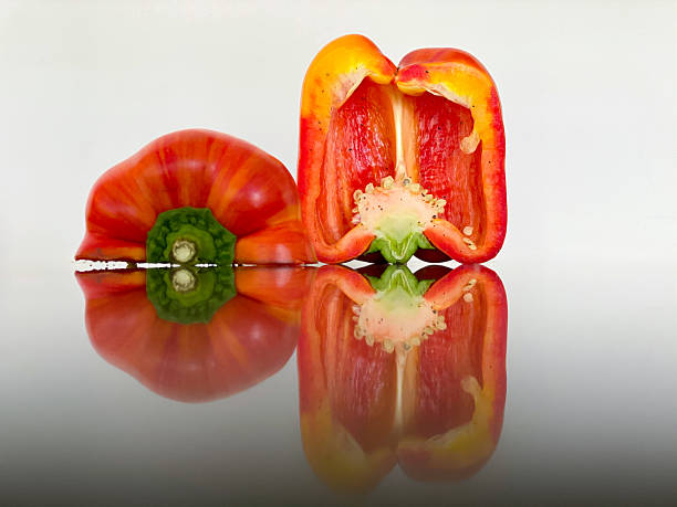 A vibrant red bell pepper is cut in half, revealing its juicy flesh and seeds. The smooth, shiny surface reflects the colorful vegetable, emphasizing its freshness and texture.