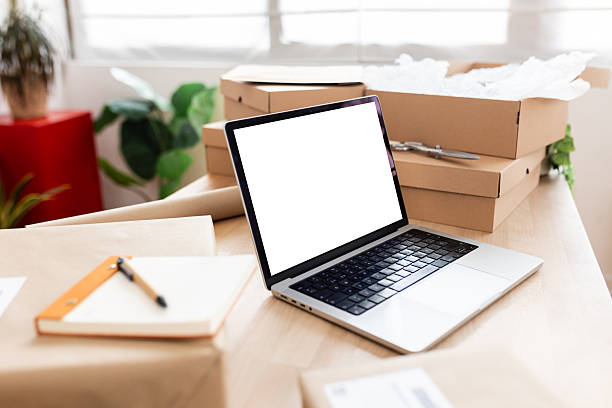 istock Laptop with blank screen, cardboard boxes, packing materials, and notebook on a desk 2222150337