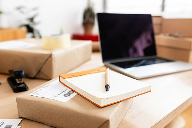 istock Notebook and pen resting on a package ready for shipping, with a laptop and other packages in the background, in a home office setting 2222151267
