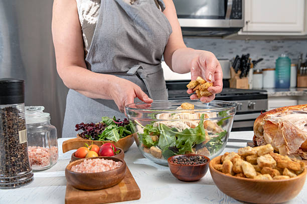 Cooking Caesar salad. Cook adds crackers to glass bowl with salad in  home kitchen