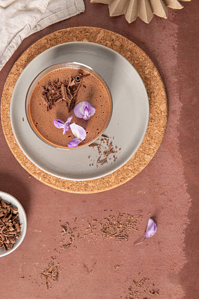istock An overhead view captures a single creamy chocolate mousse in a glass, styled on plates with a cork placemat, bowl of shavings, and decorative paper fan. 2222166320