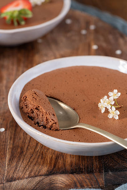 istock Creamy chocolate mousse in a white bowl, a golden spoon taking a bite, garnished with delicate white blossoms, resting on a warm wooden surface 2222166425