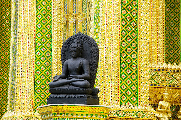 This image features a serene Buddha statue crafted from black stone, set against a vibrant backdrop of intricate gold and colorful patterns. Ideal for themes of spirituality and cultural heritage.