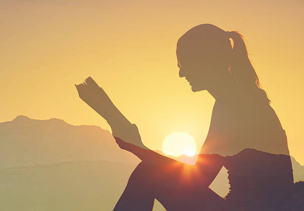 Woman reading book at sunset.
