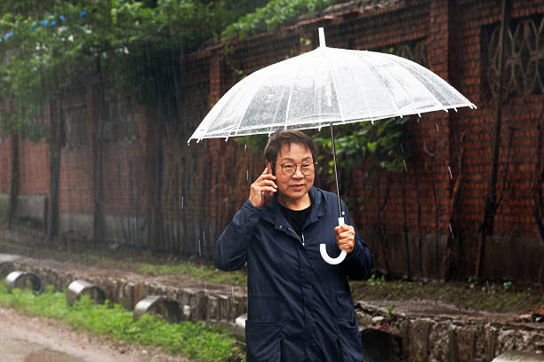 An elderly Asian woman is using her mobile phone in the rain.
