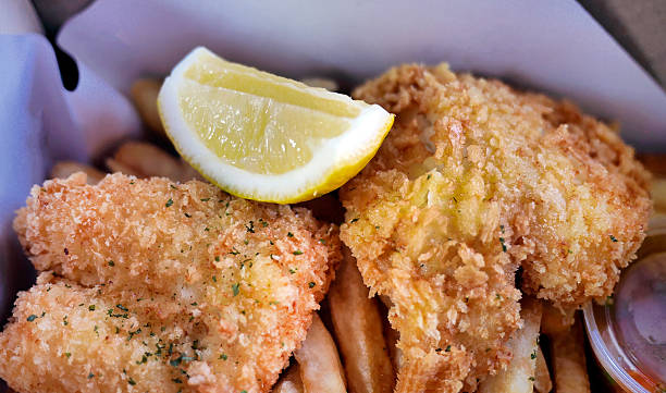 istock Classic Traditional English or British culinary delight Fish and Chips, golden deep fried fish with Lemon wedges in a paper box for takeaway as Lunch Box 2222193849