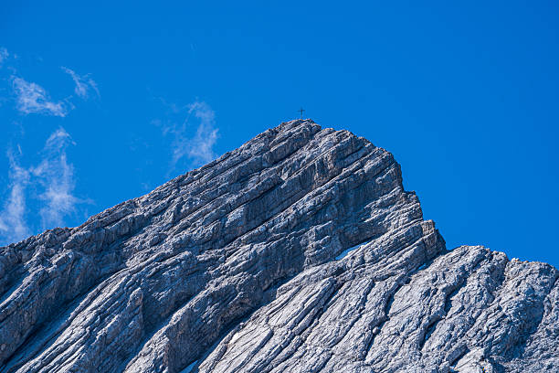 Dramatic view of the majestic Alpspitze mountain peak near Garmisch-Partenkirchen, Germany, captured under clear blue skies. The iconic pyramid-shaped summit rises sharply above lush alpine meadows and rugged rock formations, with panoramic views of the Wetterstein range. A perfect representation of Bavarian alpine beauty, ideal for nature, travel, and outdoor adventure themes.