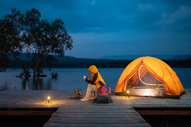 istock A woman sits on a dock by a lake with a tent and a backpack. She is reading a book 2222199867