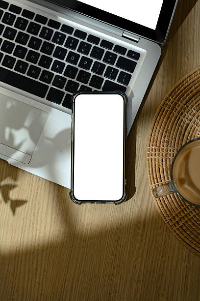 istock Flat lay of smartphone with blank screen on wooden table with coffee cup and soft sunlight shadows 2222200437