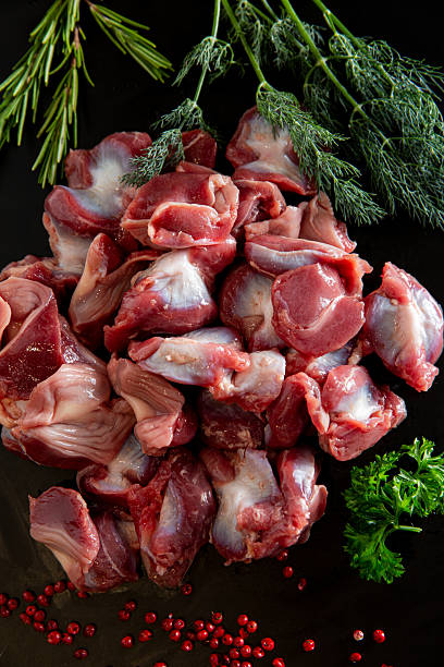 istock Flat lay of cleaned raw chicken gizzards on a black surface, decorated with peppercorns and greens. Rich in flavor, popular in traditional dishes. 2222202282