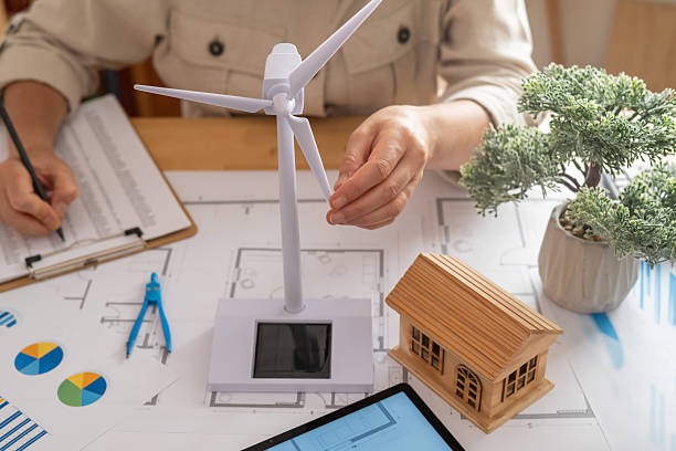 istock Engineer is working on a project involving renewable energy and sustainable solutions for future houses, using a small wind turbine model and a wooden house model 2222204555