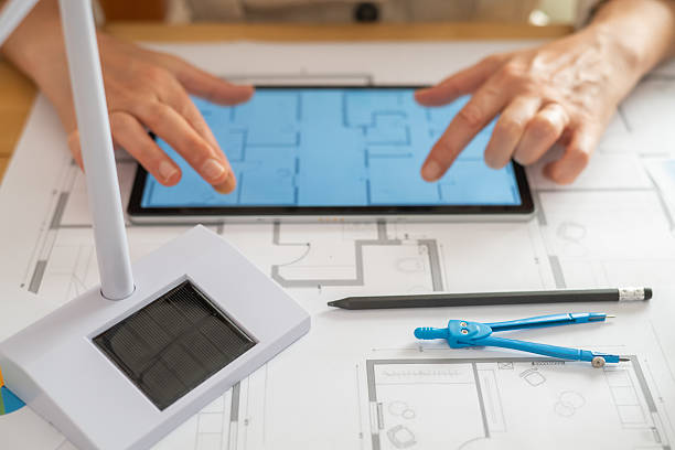 istock Engineer using a digital tablet to review blueprints for a sustainable building project, with nearby models of a solar panel and wind turbine emphasizing renewable energy 2222204568