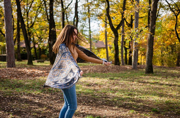 Beautiful white caucasian girl with blue eyes among trees in the forest on a sunny autumn day. The forest was full of brown fallen leaves on the ground.