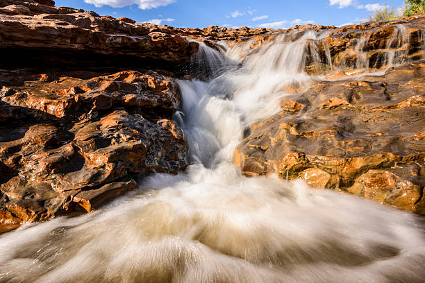Crystal-clear water flows gracefully over rugged rocks in a tranquil landscape. Sunlight illuminates the scene, creating a peaceful atmosphere in nature.