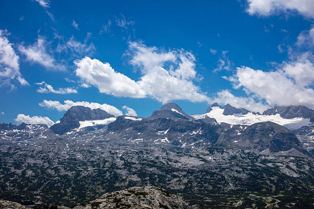 Summer Austria. Rocky Alpine mountains with snow caps on a sunny day and clouds in the blue sky
