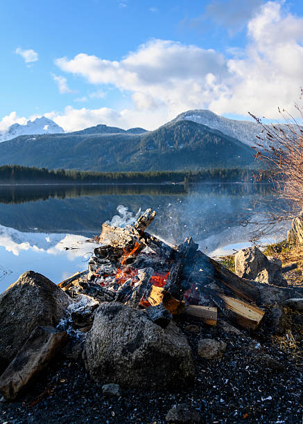 istock Fire glowing by a tranquil lake with mountains in the background on a sunny day 2222211591