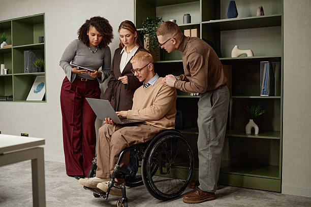 istock Young Caucasian Man with Disability Using Laptop Surrounded by Diverse Colleagues 2222215015