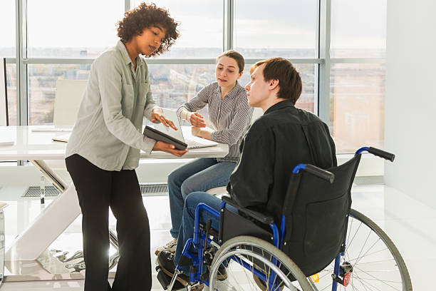 istock Teamwork brainstorm. Diverse multiracial colleagues man in chair for people with disability working together. Group of people sitting in creative office discussing business. Young professional team. 2222216861