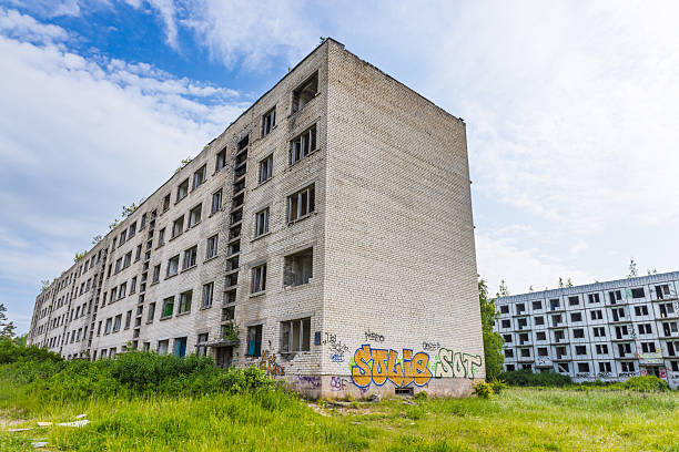 Overgrown ghost village buildings at Irbene military town, Latvia. Empty concrete flats and wild meadow create eerie lost place scene. Irbene, Latvia, 18 June 2025