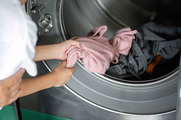 istock Laundry and Learning. A mother assists her son with loading clothes into the washing machine. 2222225476