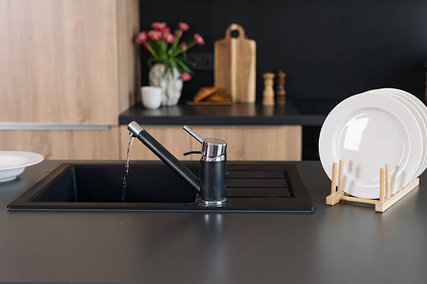 istock Modern kitchen sink on sleek black countertop with water flowing 2222230215