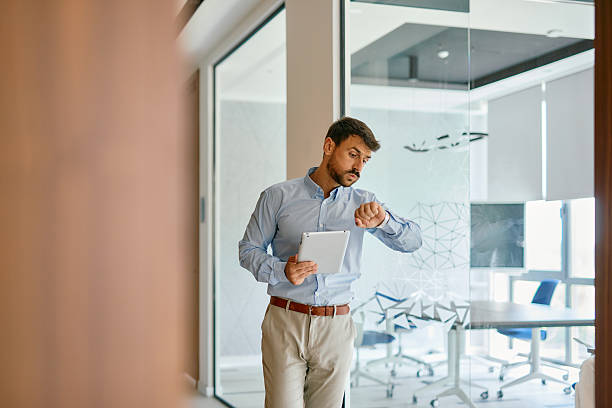 istock Businessman checking time while walking in office corridor holding tablet 2222230763