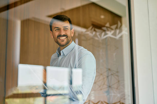 istock Smiling businessman holding digital tablet looking through modern office glass 2222230776