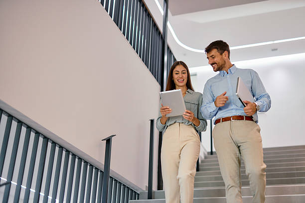 istock Business partners walking down the stairs and using digital tablet in modern office 2222231034