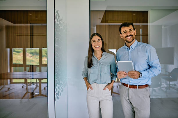 istock Smiling business partners standing in modern office holding tablet 2222232235