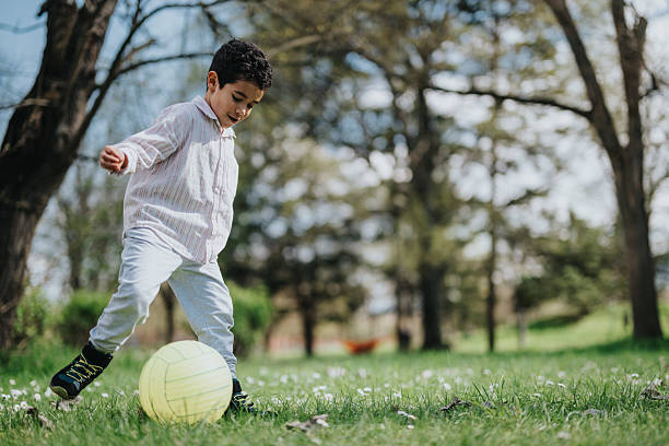 istock Young boy playing with a ball in a sunny outdoor park setting 2222233756