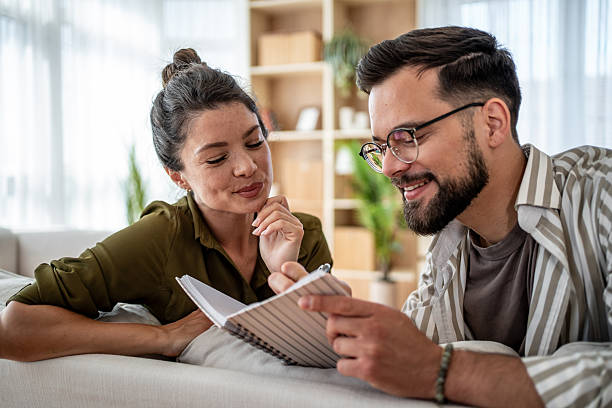 istock Young couple lying on sofa writing together in notebook, planning and sharing ideas 2222245829