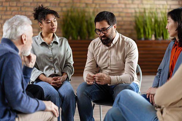 diverse group of people sharing problems during therapy session - groepstherapie stockfoto's en -beelden