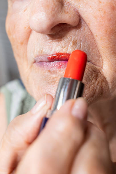 Close-up of a senior woman applying bold red lipstick, emphasizing the beauty and self-care practices that flourish at any age, celebrating confidence and personal style