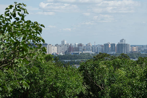 istock A vibrant city skyline is visible beyond lush greenery, with tall buildings reflecting sunlight under a bright sky. The tranquil scene merges urban development with nature, creating harmony 2222253262