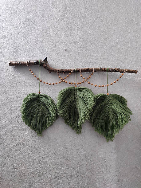 istock Three green macrame feathers on tree branch with beads wall hanging on gray textured wall background. Boho interior handmade wall decor, craft ideas, yarn decorative home decoration. 2222257566